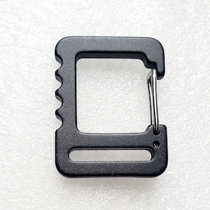 Op de afbeelding: Zwarte metalen D-ring met een zilveren lus. De D-ring heeft een getextureerd oppervlak en een klein gaatje aan de onderkant.