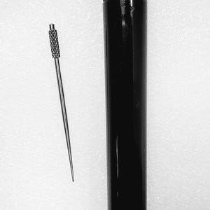 May include: A black, cylindrical container with a textured cap and a thin, silver tool with a textured handle. The tool is positioned next to the container on a white surface. The items appear to be for a specific craft or hobby.