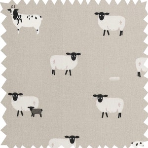 A gray throw pillow with a white border and a repeating pattern of black-faced sheep on a light gray background. Featuring the Sophie Allport Sheep fabric. The pillow is on a wood surface.