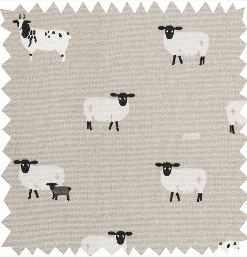 A gray throw pillow with a white border and a repeating pattern of black-faced sheep on a light gray background. Featuring the Sophie Allport Sheep fabric. The pillow is on a wood surface.