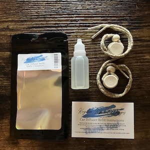 May include: A set of car diffuser refills with instructions. The set includes two brown and white string car diffusers, a clear glass bottle of refill oil, and a black resealable bag with the text "Car Diffuser Refill Apple Cinnamon".