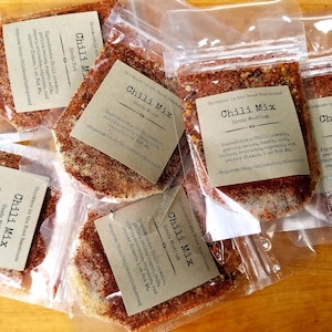May include: Five clear plastic bags filled with a brown chili mix. Each bag has a brown label with the text "Chili Mix" and the heat level: "Mild", "Medium", or "Hot". The labels also include the ingredients and the Etsy shop name: "Chickens in the Road Bakehouse".