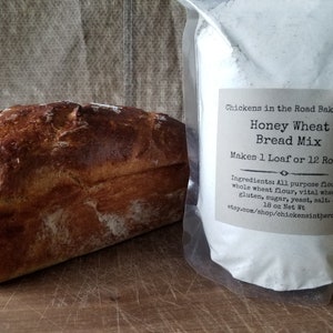 May include: A bag of Honey Wheat Bread Mix from Chickens in the Road Bakehouse. The bag contains 18 ounces of mix and makes 1 loaf or 12 rolls. The mix contains all-purpose flour, whole wheat flour, vital wheat gluten, sugar, yeast, and salt. The bag is next to a loaf of freshly baked bread.