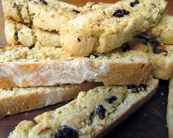 May include: A close-up of a stack of biscotti cookies with a light brown colour and a slightly grainy texture. The cookies are topped with dried cranberries and are arranged on a wooden surface.