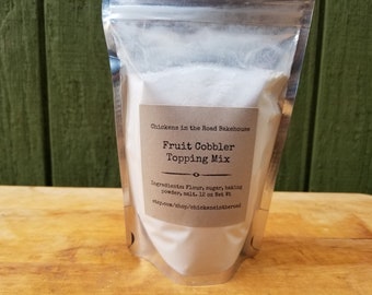May include: A silver pouch with a white label that reads "Chickens in the Road Bakehouse Fruit Cobbler Topping Mix" and lists the ingredients as "Flour, sugar, baking powder, salt. 12 oz Net Wt." The label also includes the website "etsy.com/shop/chickensintheroad".