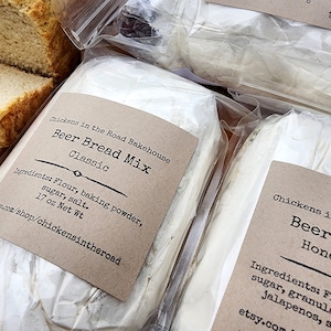 May include: Close-up of packaged Beer Bread Mix from Chickens in the Road Bakehouse. The label reads "Classic" and lists ingredients. Sliced bread is visible on the left. The net weight is 17 oz.
