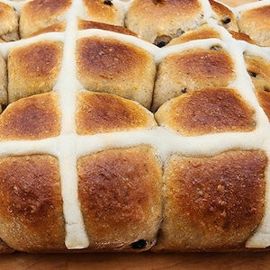 May include: A close-up of a tray of freshly baked hot cross buns with a white icing glaze. The buns are golden brown and have a slightly crispy crust.