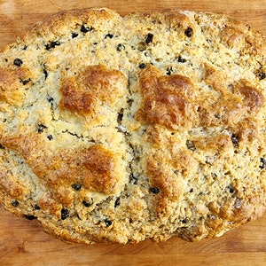 May include: A round loaf of Irish soda bread with a golden brown crust and dark raisins throughout.