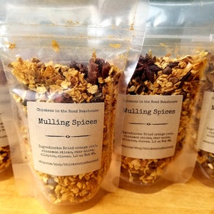 May include: Four small clear plastic bags filled with dried orange peel, cinnamon sticks, star anise, cloves, and allspice. Each bag has a brown label that reads "Chickens in the Road Bakehouse Mulling Spices" and lists the ingredients. The label also includes the website address "shop.com/shop/chickensintheroad".