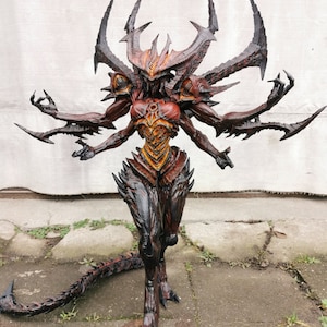 May include: A detailed demon statue with multiple arms and a threatening appearance. The figure is mainly red, black, and orange, with sharp, angular features, including horns and claws. The statue has a long tail and is posed in a dynamic stance.