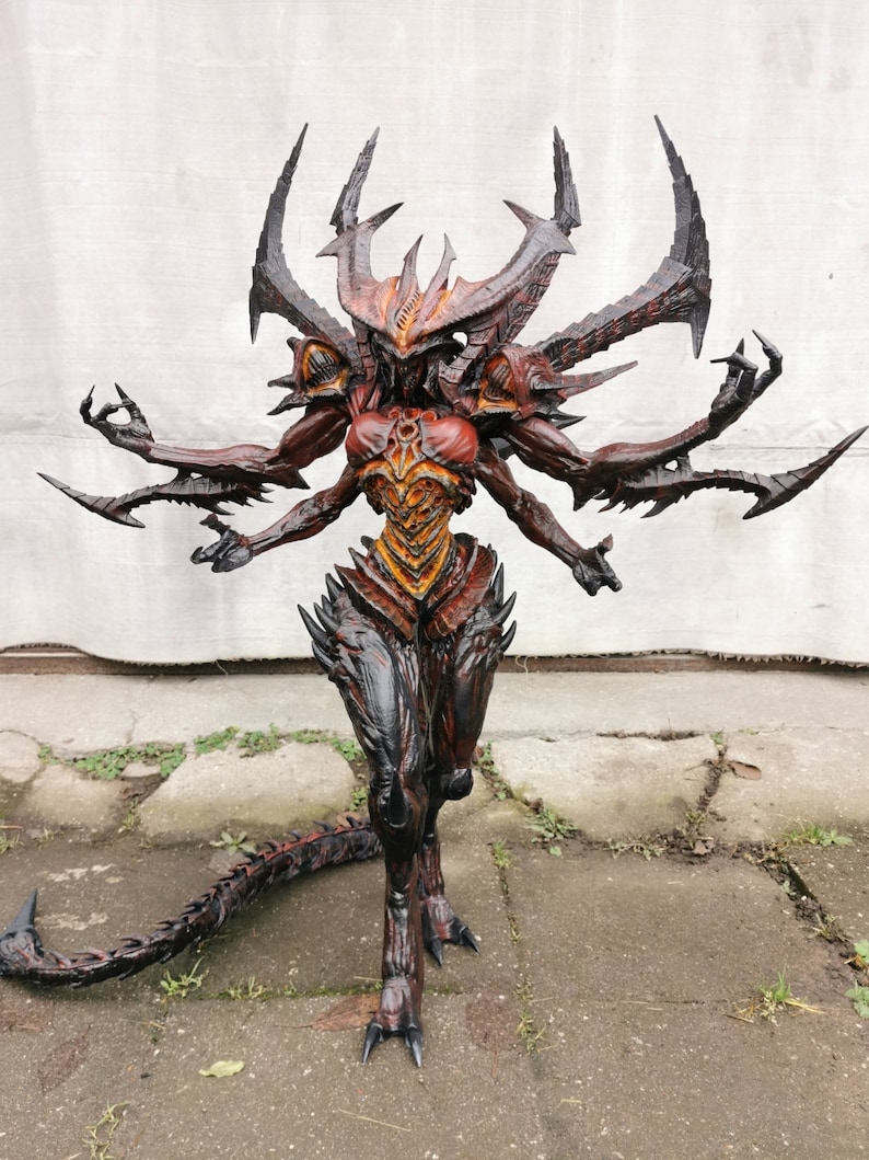 May include: A detailed demon statue with multiple arms and a threatening appearance. The figure is mainly red, black, and orange, with sharp, angular features, including horns and claws. The statue has a long tail and is posed in a dynamic stance.