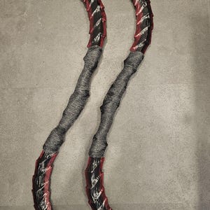 Pode incluir: Dois objetos curvos em forma de lâmina com detalhes em vermelho e preto. As lâminas têm uma borda serrilhada e são conectadas a cabos cinza enrolados. Os objetos são exibidos em um fundo cinza.