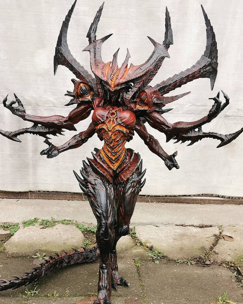 May include: A detailed sculpture of a demonic figure with multiple arms and a tail. The figure is predominantly red, black, and orange, with sharp, spiky features and a menacing expression. The sculpture appears to be a fantasy or gaming-themed collectible.