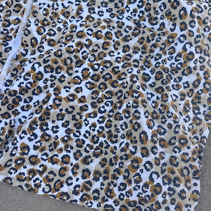 May include: A piece of fabric featuring a repeating leopard print pattern. The design consists of dark charcoal gray and mustard yellow spots outlined in black, set against a stark white background, creating a high-contrast animal print textile.