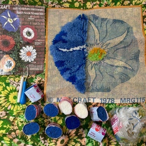 May include: A latch hook craft kit with a blue and white flower design. The kit includes yarn, a mesh canvas, and a hook. The kit is labeled "Millcraft 1978 MRGT115".