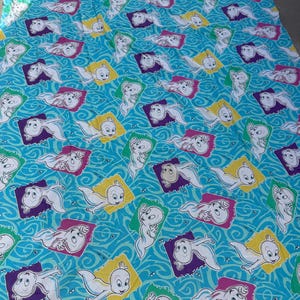 Op de afbeelding: Een lichtblauw laken met een herhaald patroon van het stripfiguur Casper het vriendelijke spook. Elke Casper staat in een kleurrijk vierkant, met een golvende blauwe achtergrond.