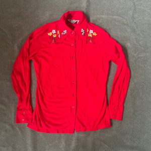 May include: A red long-sleeved button-up shirt with embroidered floral details on the collar. The shirt has a classic collar and a button-up front.
