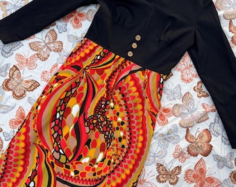 May include: A black long-sleeved dress with a fitted bodice and a colorful, abstract print skirt. The skirt features swirls of red, orange, yellow, and brown.