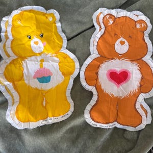 May include: Two Care Bear fabric patches. One is yellow with a cupcake graphic, the other is orange with a heart. Both have white borders and the text "LEAVE OPEN FOR STUFFING".
