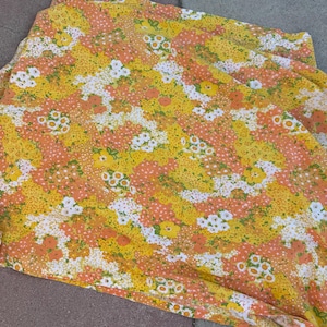 May include: A fabric sheet featuring a dense, repeating floral pattern in shades of bright yellow, soft orange, and white. The design consists of various small flower clusters and petals distributed across the entire surface of the textile material.