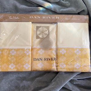 May include: A packaged set of Dan River fine muslin pillowcases and sheets. The sheets are a pale yellow with a yellow and white diamond pattern border. The packaging is brown with the Dan River logo and text.