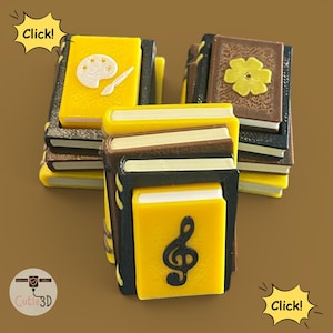 May include: A collection of miniature books with yellow, brown, and black covers. Some books feature art-related icons like a palette and brush, while others display a musical treble clef or a flower. The books are stacked in small piles.