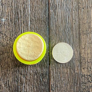 K&ouml;nnte beinhalten: Ein gelb-beiges kreisf&ouml;rmiges Objekt mit strukturiertem Design, neben einer M&uuml;nze. Das Objekt scheint ein Bastel- oder Dekorationsartikel zu sein, m&ouml;glicherweise ein Stempel oder eine Form. Die M&uuml;nze dient als Gr&ouml;&szlig;enreferenz.