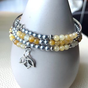 May include: A multi-strand wrap bracelet featuring alternating rows of yellow translucent beads and metallic silver beads. The bracelet includes small silver-toned spacers and a silver-colored lotus flower charm hanging from the center.