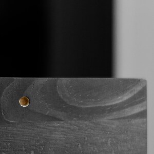 Puede incluir: Primer plano de una superficie de madera oscura con un peque&ntilde;o tornillo redondo dorado en el centro.