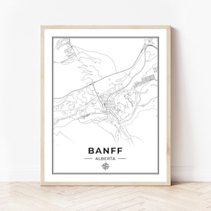 Peut inclure: Une carte de Banff, en Alberta, au Canada, en noir et blanc, avec des lignes. La carte est encadrée dans un cadre en bois clair et comporte une rose des vents au centre inférieur.
