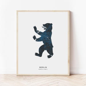May include: A framed print of the Berlin bear, a black silhouette of the bear with a blue map pattern, against a white background. The text "BERLIN 52.5200° N, 13.4050° E" is printed below the bear.
