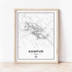 May include: A black and white map print of Kanpur, India, in a light wood frame. The map shows the city's streets and landmarks. The city name and country are printed below the map, along with a compass rose.