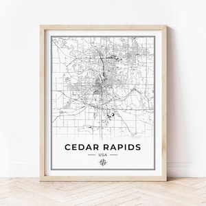 May include: Black and white map print of Cedar Rapids, Iowa, USA. The map shows the city streets and landmarks. The print is framed in a light wood frame.