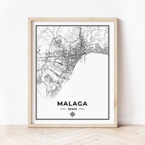 May include: Black and white line art map print of Malaga, Spain. The map shows the city streets and coastline. The city name and country are printed below the map with a compass rose.