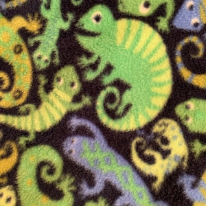 May include: A black fabric with a repeating pattern of green, yellow, and blue lizards. The lizards are stylized and have a cartoonish appearance.