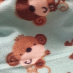 May include: A soft, blue fleece blanket with a brown monkey pattern. The blanket has a brown fleece lining.