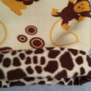 May include: A cream-colored fleece blanket with a brown, yellow, and white animal print. The blanket features a lion, a monkey, and a giraffe print.