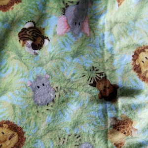 May include: A green fabric with a repeating pattern of jungle animals, including elephants, lions, tigers, and monkeys. The fabric has a soft, fuzzy texture.