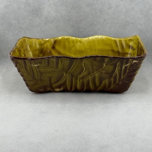May include: A rectangular, ceramic planter with a leaf design. The planter is primarily olive green with a darker brown trim and interior. The edges have a wavy design.