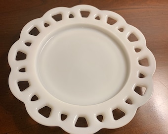 May include: White milk glass plate with a scalloped edge and a decorative cut-out design. The plate is perfect for serving desserts or snacks.