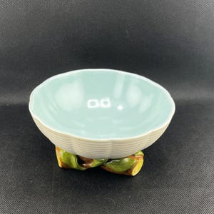 May include: A light blue ceramic bowl with a white ribbed base and a green and brown leafy base.