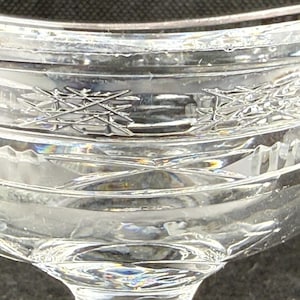 May include: Close-up of a clear, crystal glass with intricate etched designs. The glass features a detailed pattern of intersecting lines and geometric shapes, reflecting light. The stemware is likely for beverages.