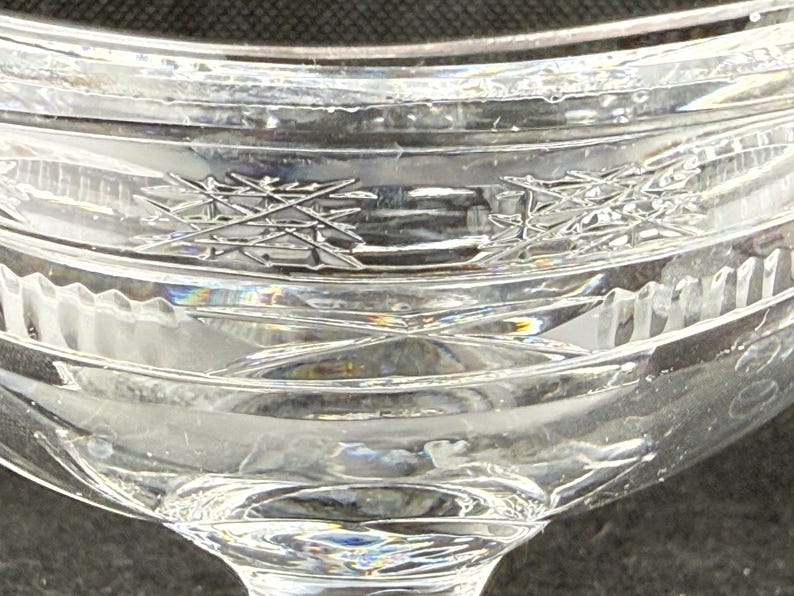 May include: Close-up of a clear, crystal glass with intricate etched designs. The glass features a detailed pattern of intersecting lines and geometric shapes, reflecting light. The stemware is likely for beverages.