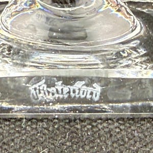 May include: Close-up of a clear glass object with a rounded top and a rectangular base. The base has etched text. The object is on a dark surface. The glass is transparent and reflects light.