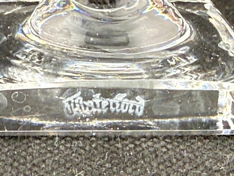 May include: Close-up of a clear glass object with a rounded top and a rectangular base. The base has etched text. The object is on a dark surface. The glass is transparent and reflects light.