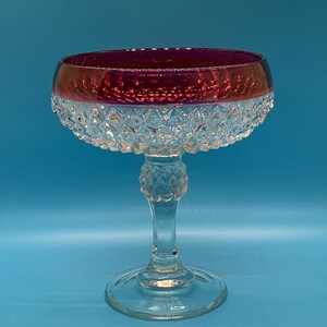 May include: A clear glass goblet with a diamond-shaped pattern on the bowl and stem. The top of the bowl is a deep burgundy red.