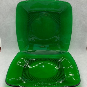 Peut inclure: Deux assiettes carrées en verre vert avec un bord noir et un motif de cercle concentrique au centre.