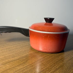 May include: A red and black saucepan with a black handle. The saucepan has a speckled red finish and a silver rim.