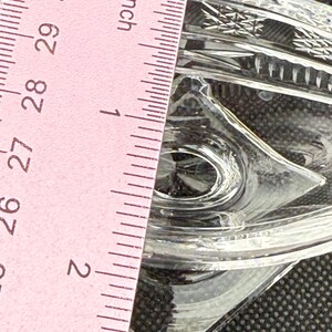 May include: Clear glass dish with diamond-shaped details. The dish is approximately 2 inches wide. The image shows a pink ruler with inch measurements. The dish has a decorative, textured pattern.