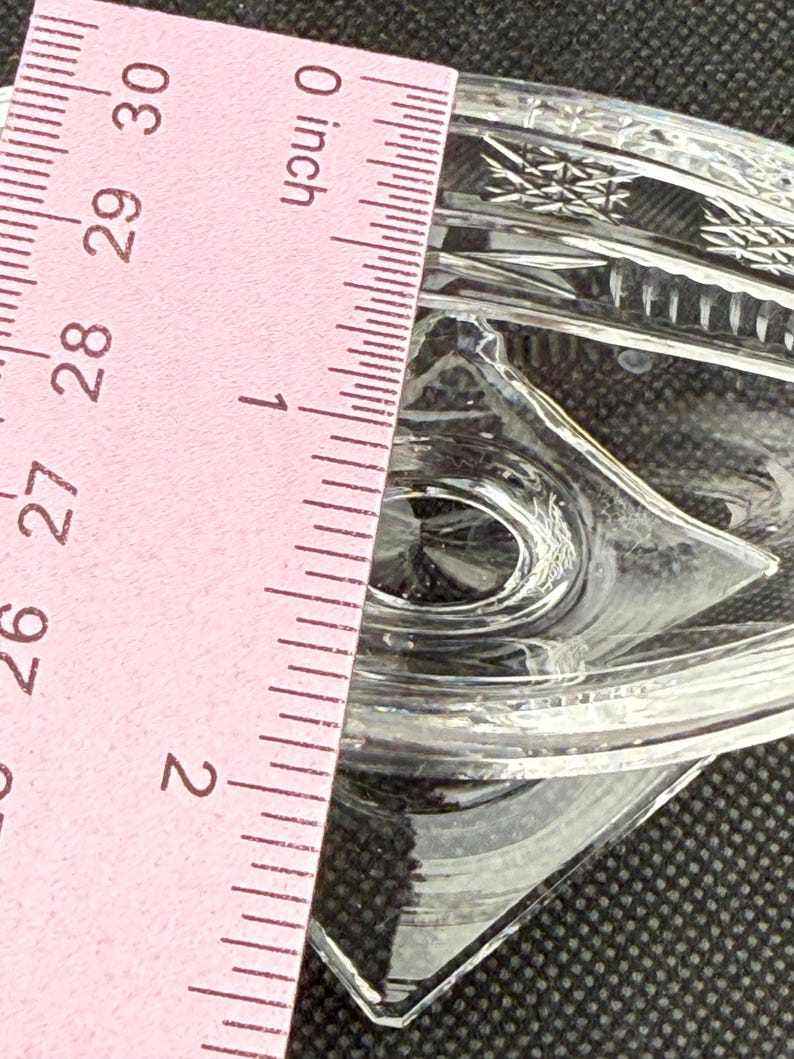 May include: Clear glass dish with diamond-shaped details. The dish is approximately 2 inches wide. The image shows a pink ruler with inch measurements. The dish has a decorative, textured pattern.